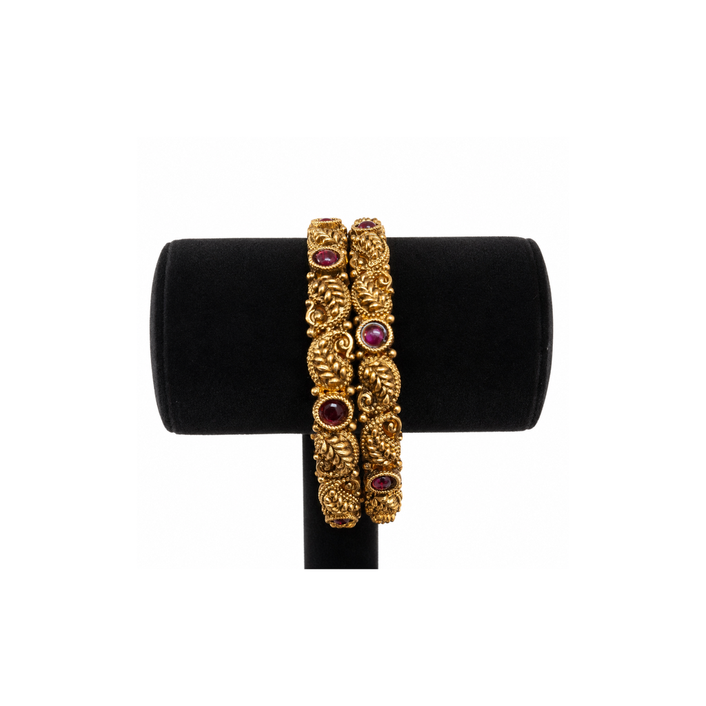 Pair of antique gold-tone paisley bangles with deep-red stones on black velvet