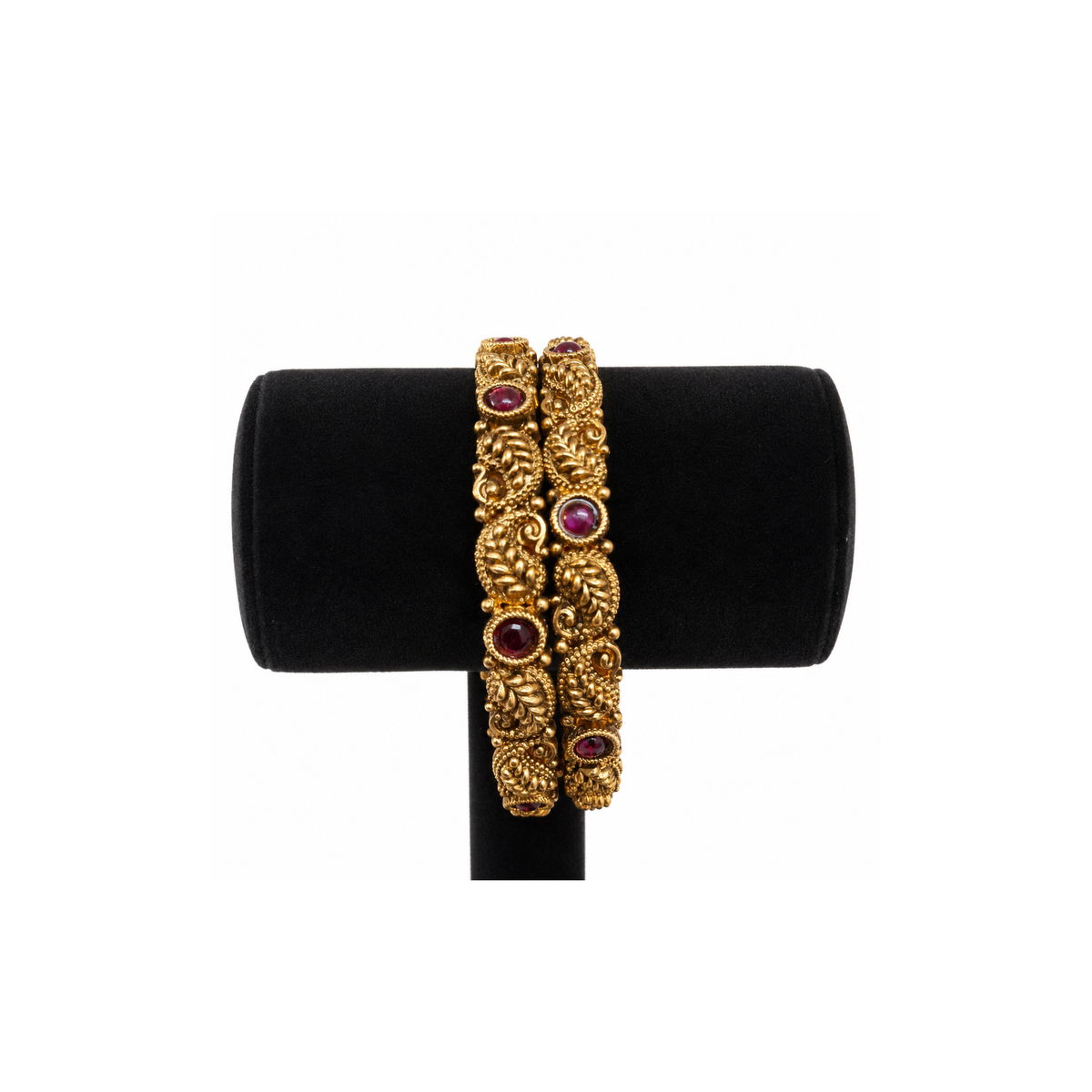 Pair of antique gold-tone paisley bangles with deep-red stones on black velvet