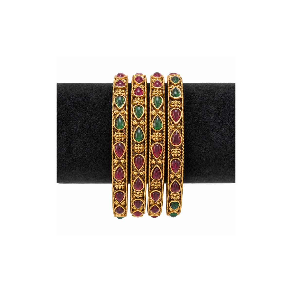 Four antique gold-tone bangles with red and green teardrop stones on black velvet