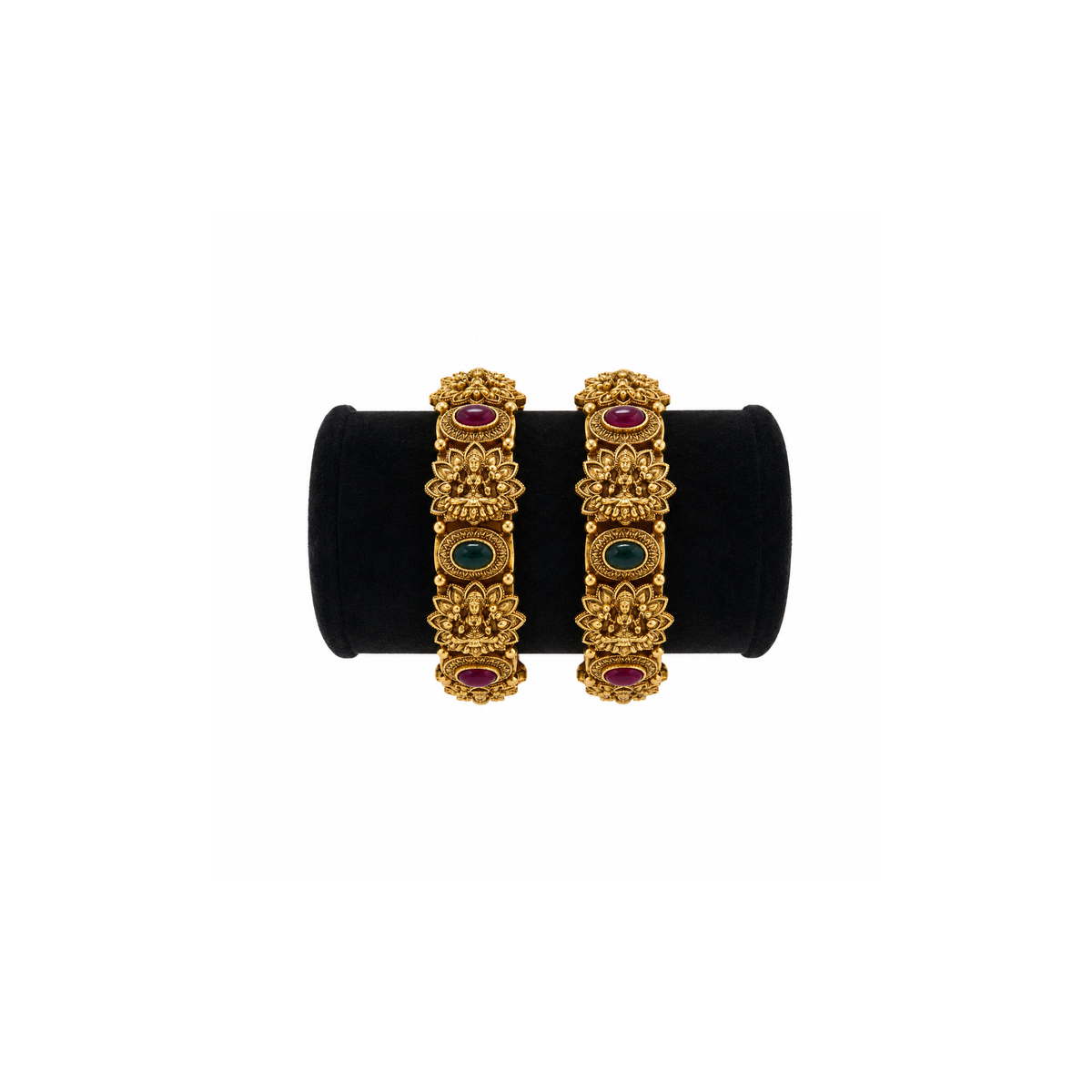 Pair of antique gold-tone Lakshmi temple bangles with red and green oval stones on a black velvet stand