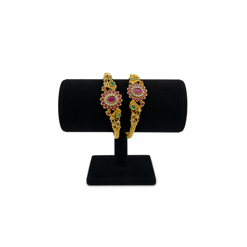 Two magenta and green floral gold-tone bangles on a black velvet stand
