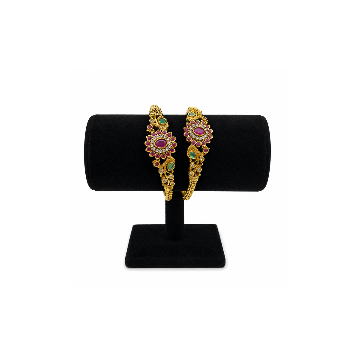 Two magenta and green floral gold-tone bangles on a black velvet stand