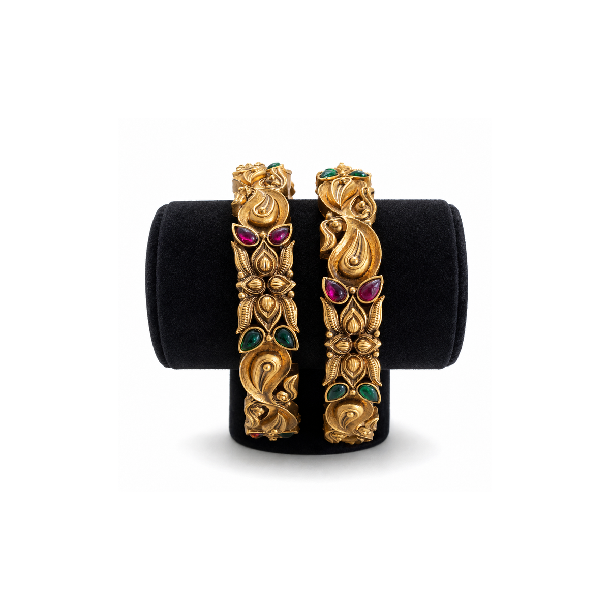 Two antique gold-tone peacock paisley bangles with ruby-pink and green stones on black velvet