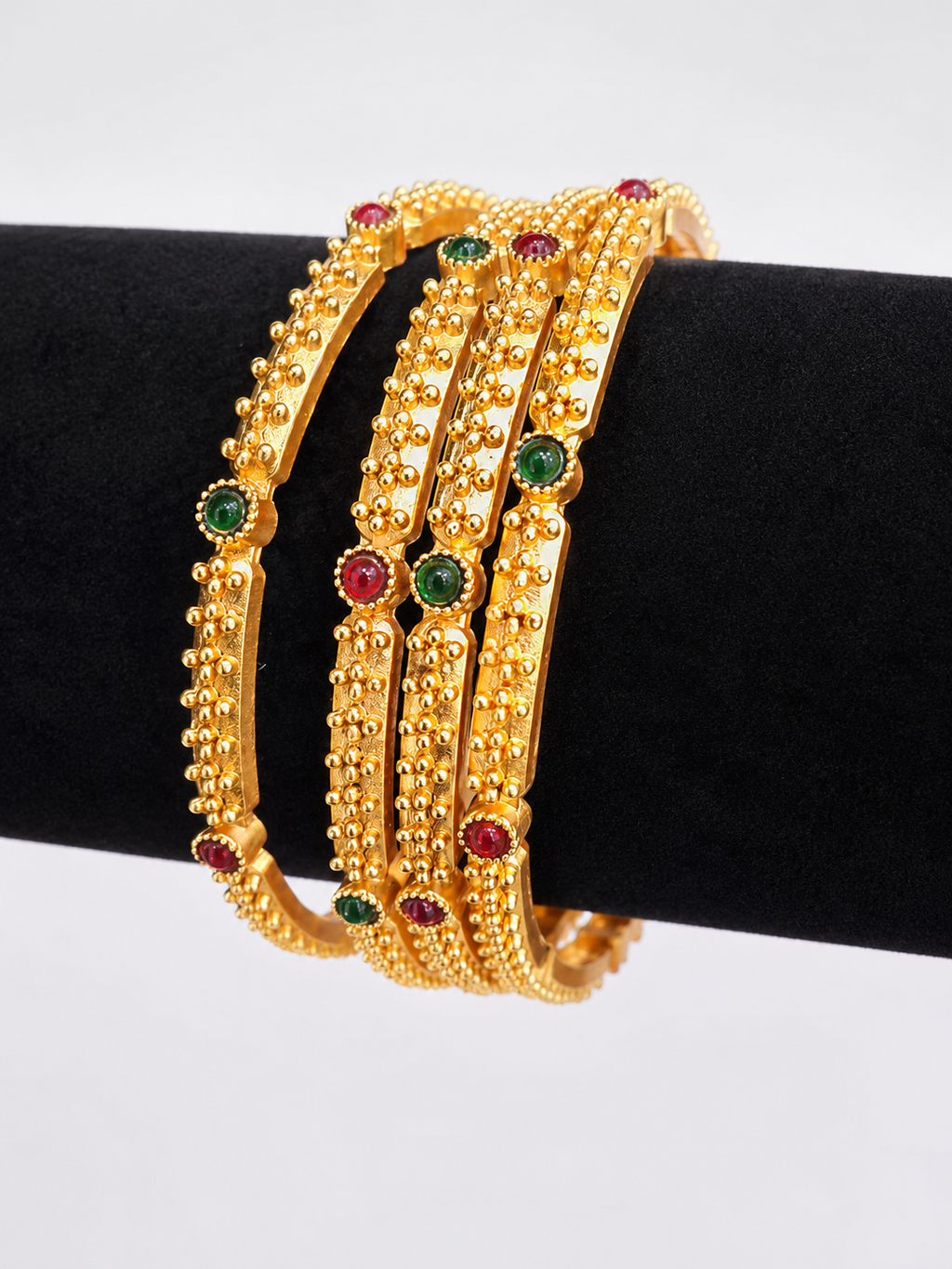 Four gold-tone textured bangles with red and green accents, angled view