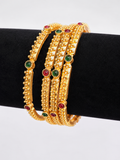 Four gold-tone textured bangles with red and green accents, angled view