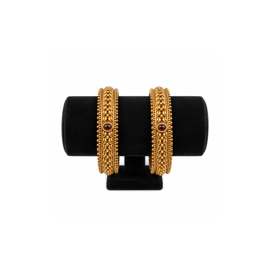 Two red stone braided antique gold-tone bangles on black velvet
