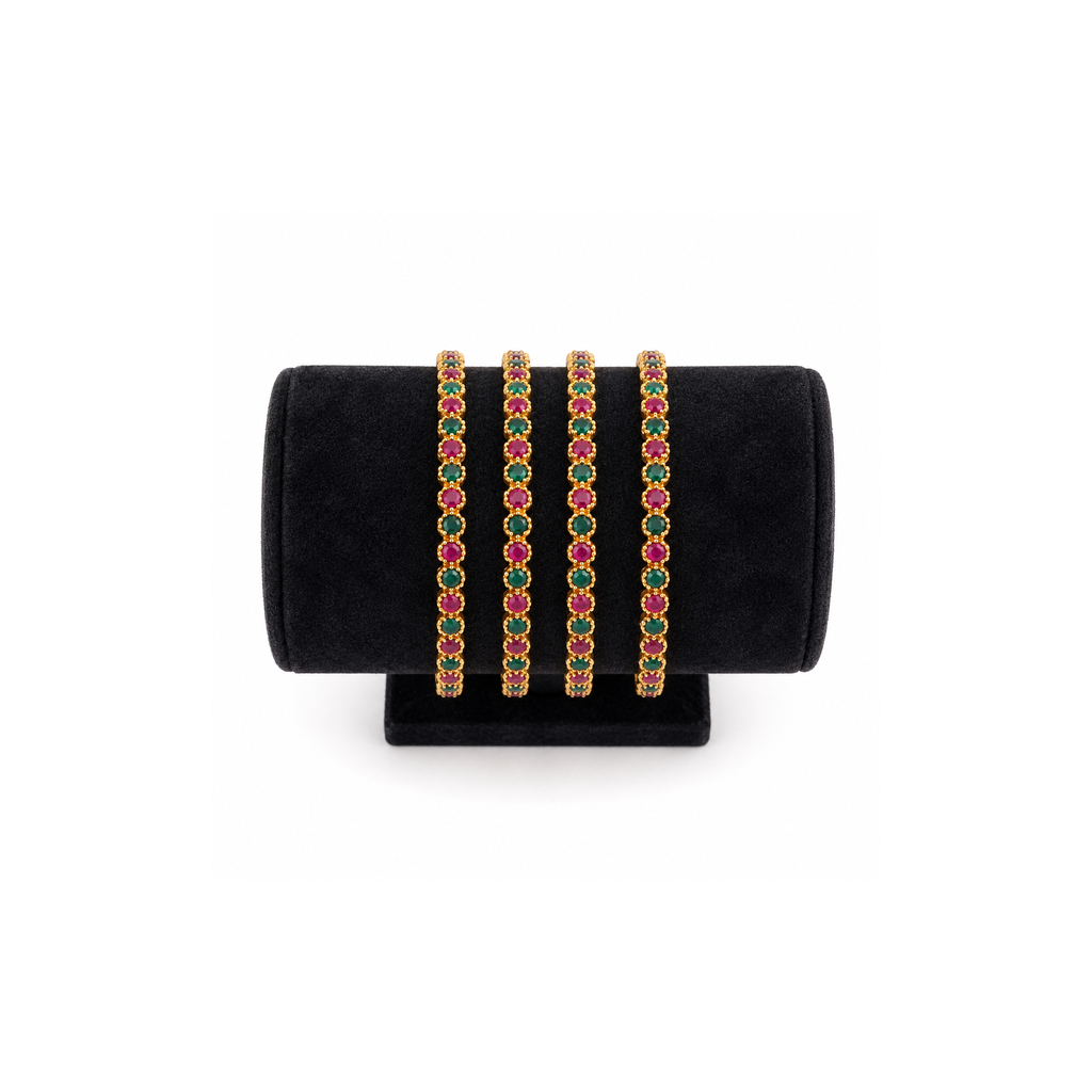 Four slim gold-tone bangles with alternating deep pink and green stones on a black velvet stand