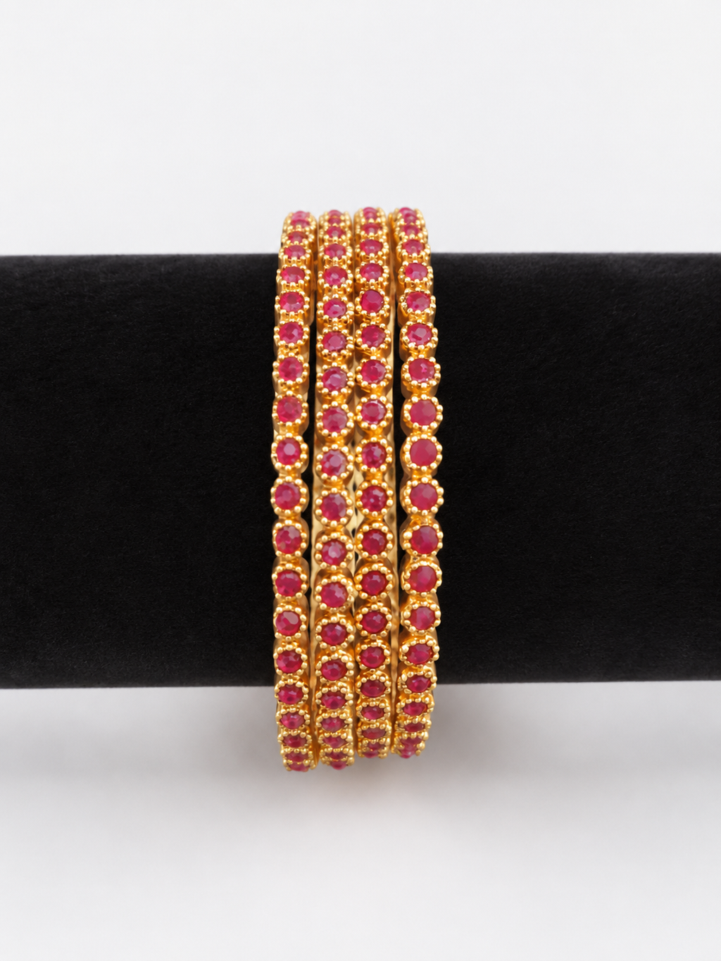 Four gold-tone bangles with round ruby-pink stones, front view