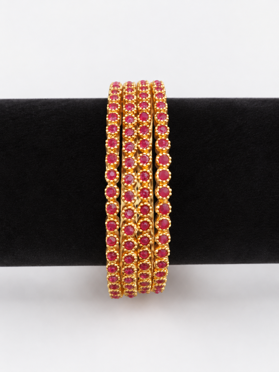 Four gold-tone bangles with round ruby-pink stones, front view