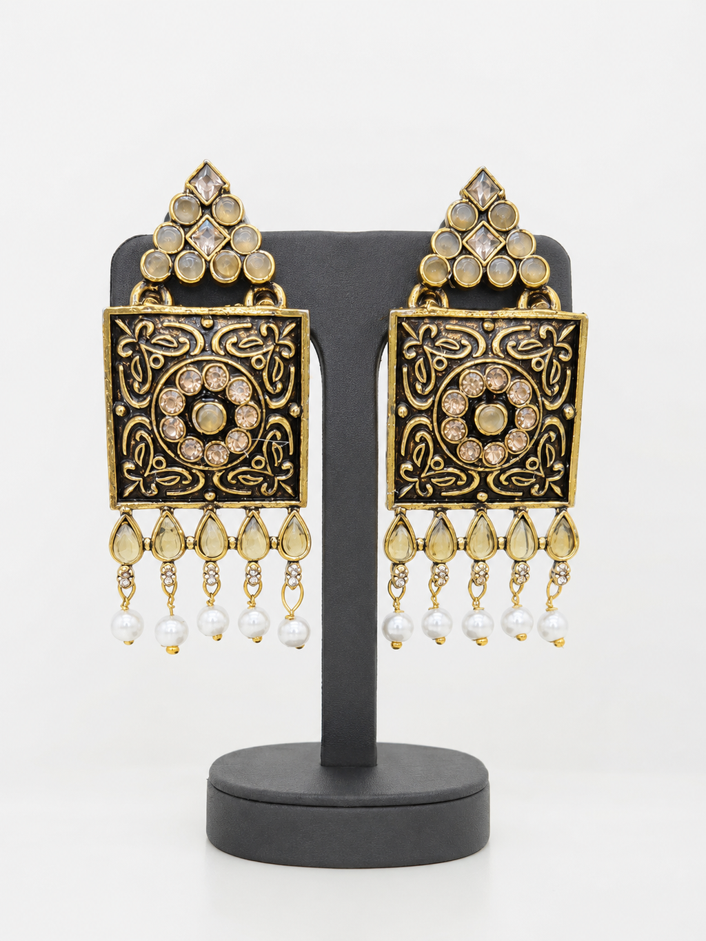 Square antique-gold statement earrings on black stand, angled view