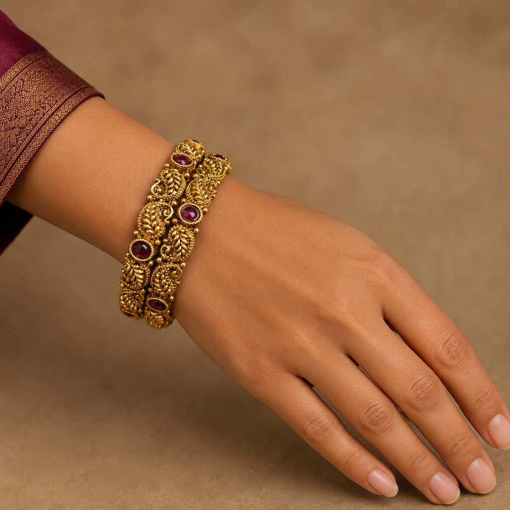 Hand wearing two antique gold-tone paisley bangles with deep-red stones