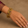 Hand wearing two antique gold-tone paisley bangles with deep-red stones