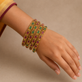 Hand wearing four antique gold-tone bangles with red and green teardrop stones