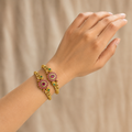 Hand wearing two magenta and green floral gold-tone bangles