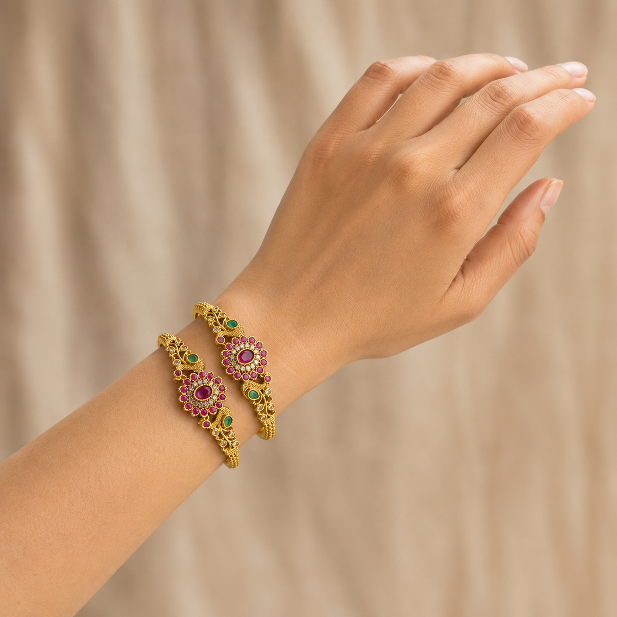 Hand wearing two magenta and green floral gold-tone bangles