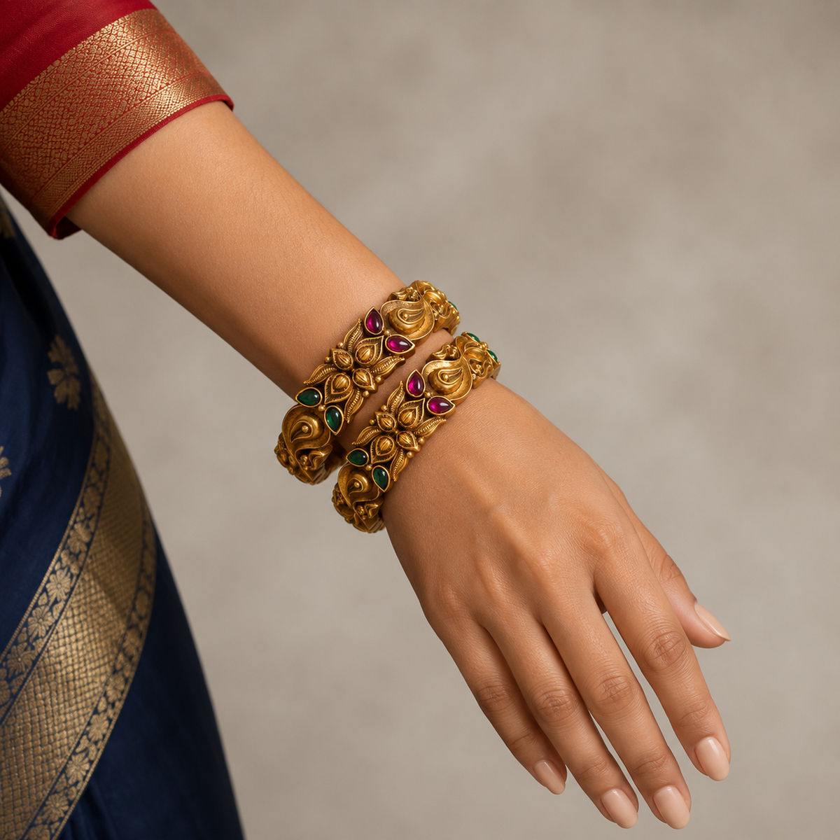 Indian hand wearing two broad gold-tone peacock paisley bangles with pink and green stones