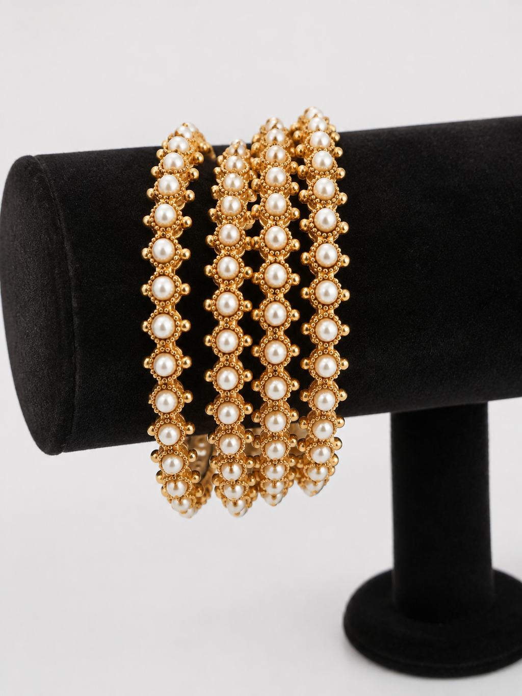 Four pearl-style gold-tone bangles on black stand, angled view