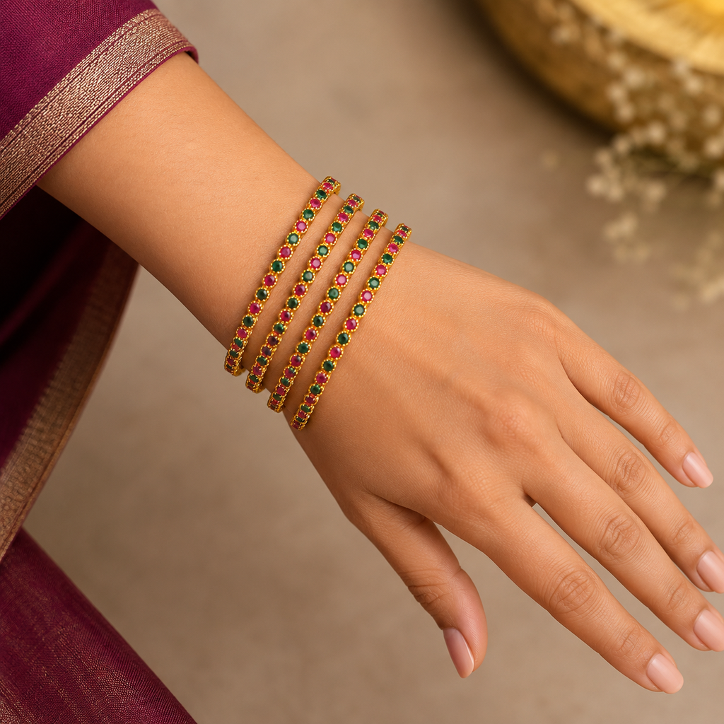 Indian hand wearing four gold-tone bangles with alternating deep pink and emerald-green stones