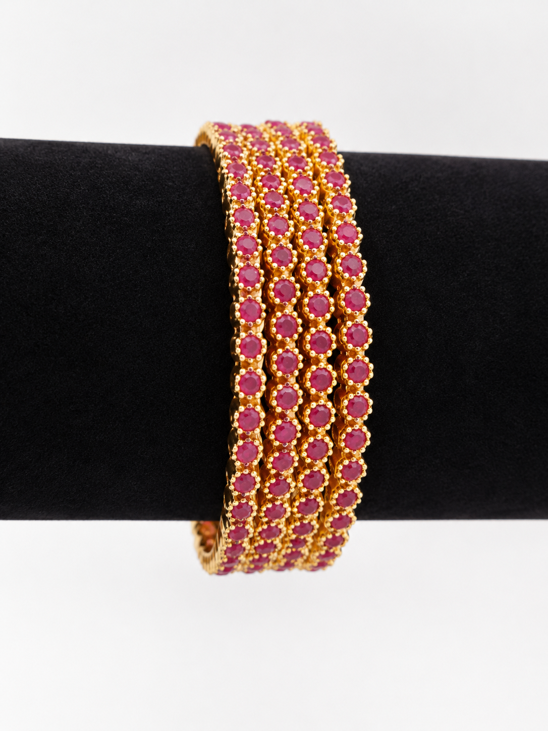 Ruby-pink stone gold-tone bangle set on black stand, angled view