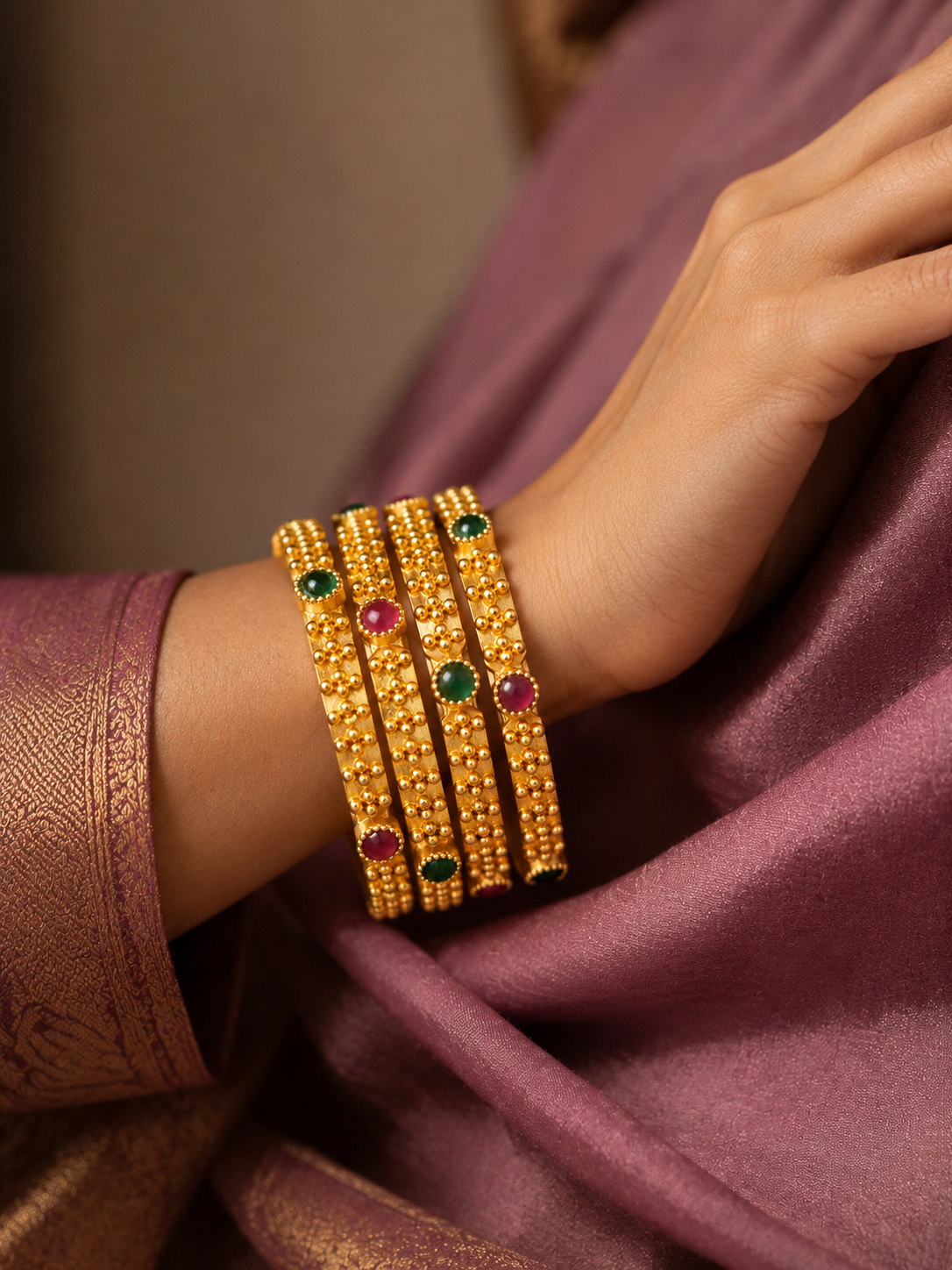 Four red and green accent gold-tone bangles worn with plum silk