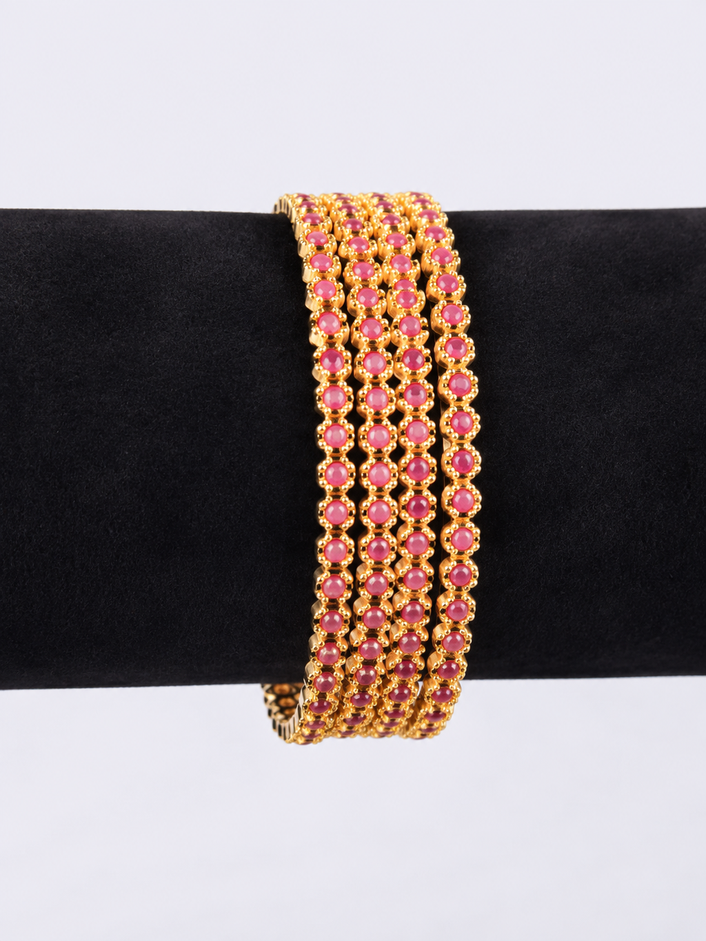 Four ruby-pink bangles showing repeating round stone settings